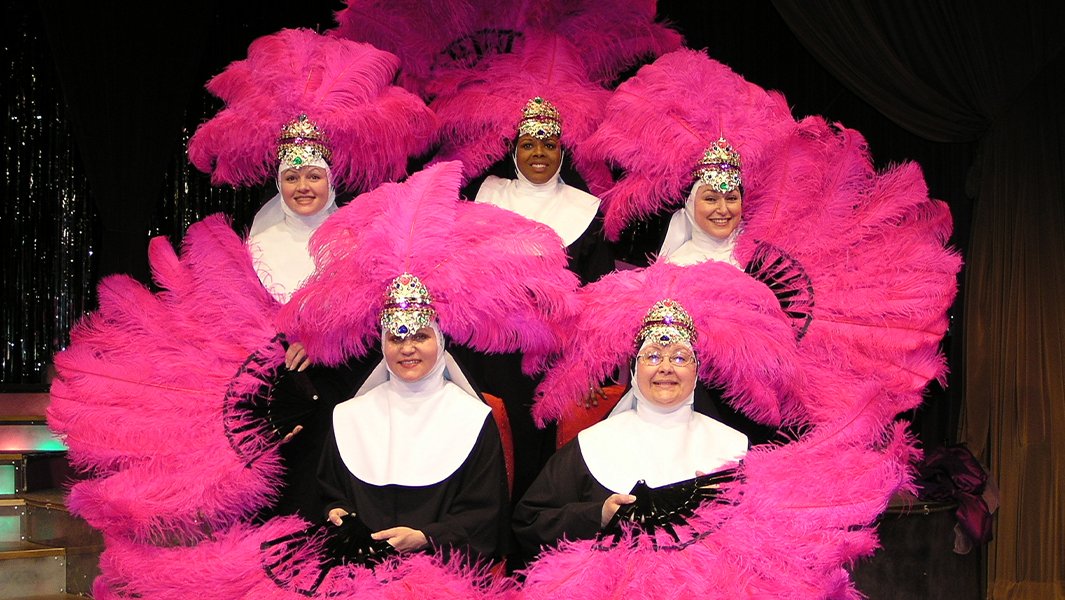 A photo of five nuns with pink feather hats and fans from Nunsensations.
